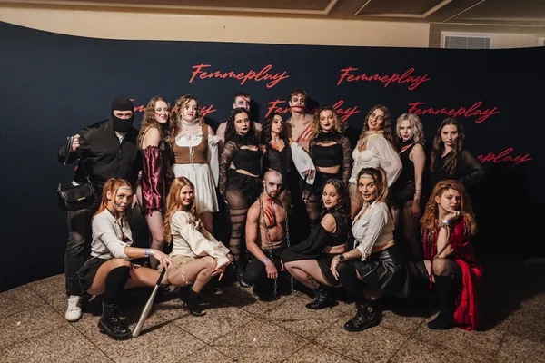 Skupina hostek v rozmanitých kostýmech u společné fotostěny