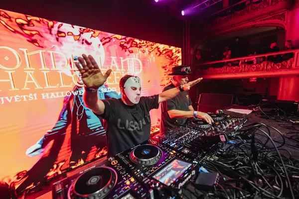 DJ za mixážním pultem se zdviženýma rukama před červenou LED scénou
